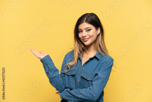 Young Russian girl isolated on yellow background extending hands to the side for inviting to come © luismolinero