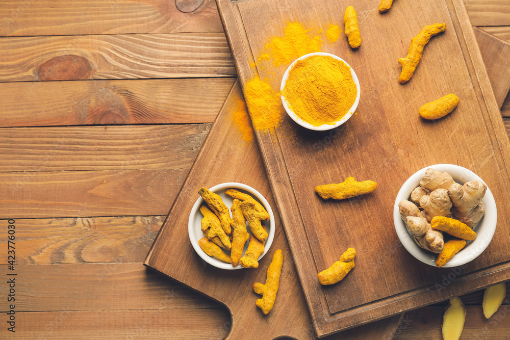 Composition with turmeric powder and roots on wooden background Composition with turmeric powder and roots on wooden background