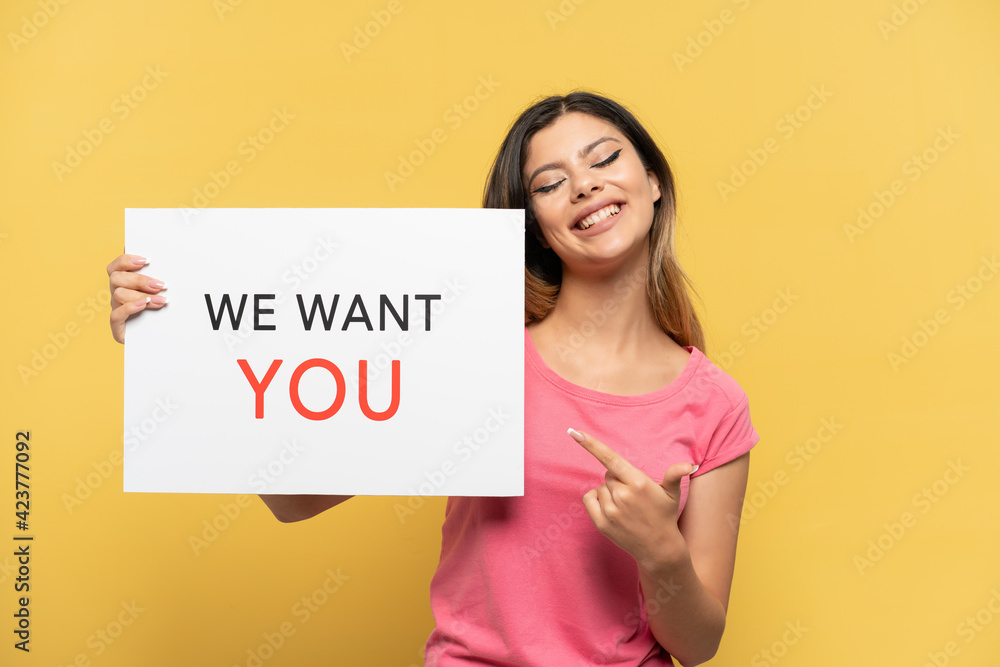 Young Russian girl isolated on yellow background holding We Want You board and pointing it Young Russian girl isolated on yellow background holding We Want You board and pointing it