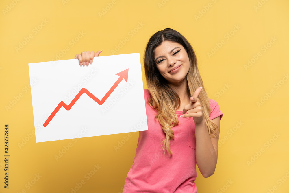 Young Russian girl isolated on yellow background holding a sign with a growing statistics arrow symbol and pointing to the front Young Russian girl isolated on yellow background holding a sign with a growing statistics arrow symbol and pointing to the front