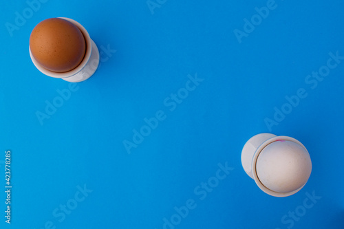 Along the edges there is a white and brown chicken egg in a stand on a blue background. Easter card concept