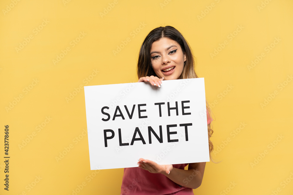 Young Russian girl isolated on yellow background holding a placard with text Save the Planet with happy expression Young Russian girl isolated on yellow background holding a placard with text Save the Planet with happy expression