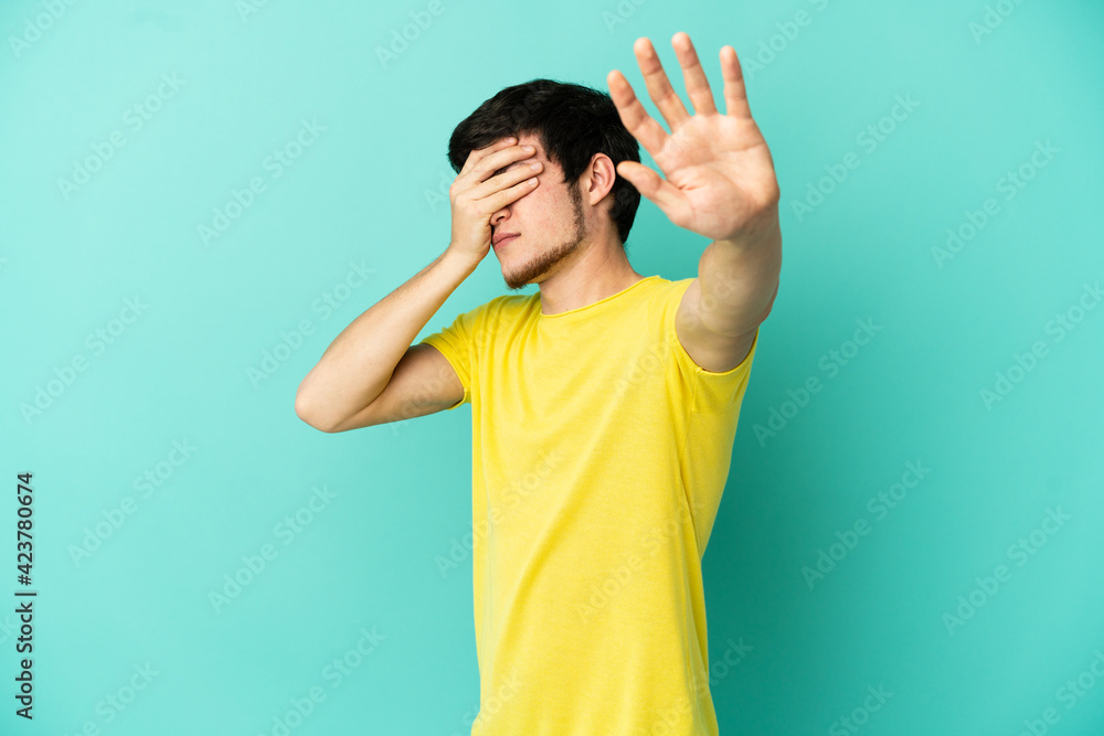 Young Russian man isolated on blue background making stop gesture and covering face Young Russian man isolated on blue background making stop gesture and covering face