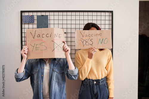 Girls hiding their faces behind the cupboard posters about covid 19 vaccine