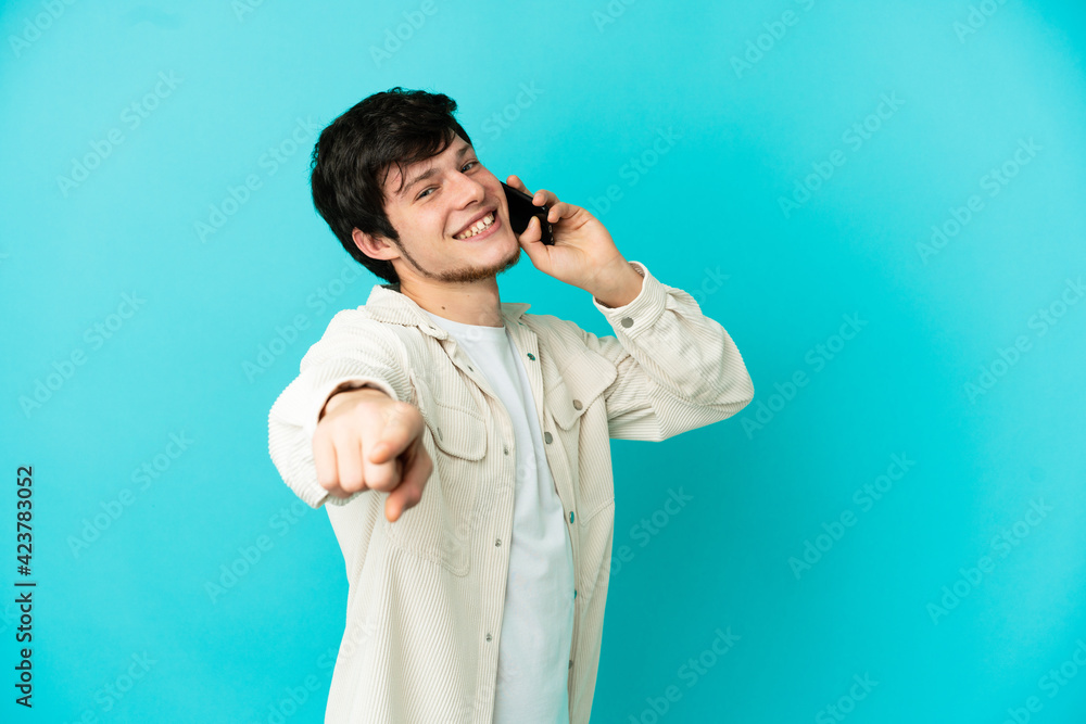 Young Russian man using mobile phone isolated on blue background pointing front with happy expression Young Russian man using mobile phone isolated on blue background pointing front with happy expression