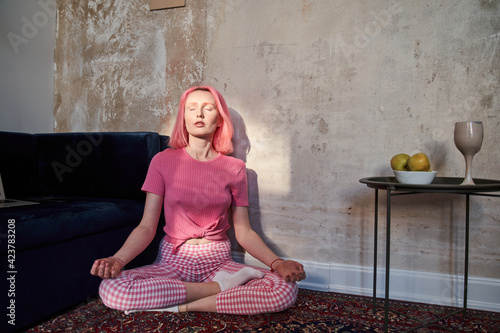 Woman with pink hair meditating at home in the morning