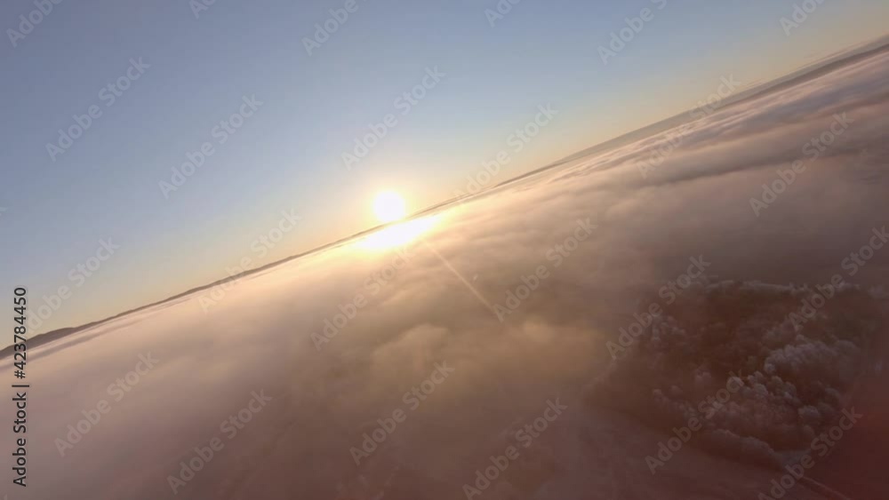 Cruising slow flight high above clouds towards the sun with mountains in the background over frozen winter wonderland landscape Cruising slow flight high above clouds towards the sun with mountains in the background over frozen winter wonderland landscape
