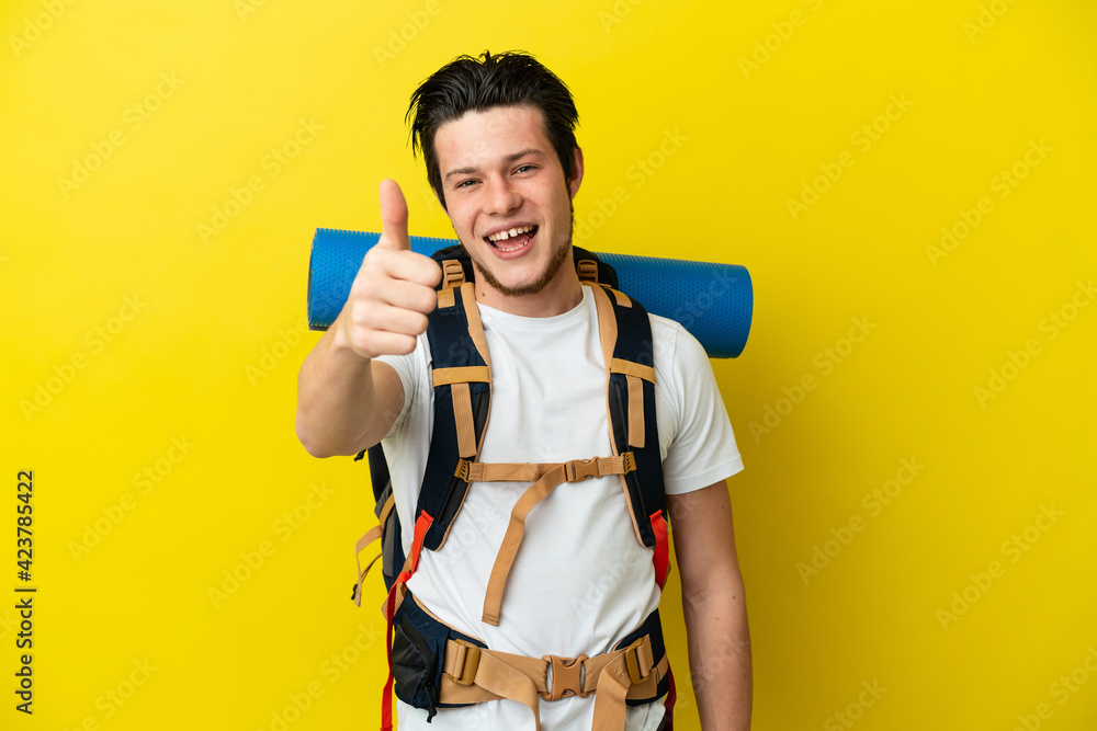 Young mountaineer Russian man with a big backpack isolated on yellow background with thumbs up because something good has happened Young mountaineer Russian man with a big backpack isolated on yellow background with thumbs up because something good has happened