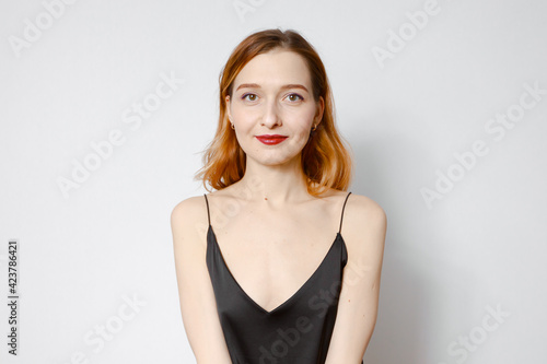Portrait of a beautiful red-haired girl in a black blouse. Light background