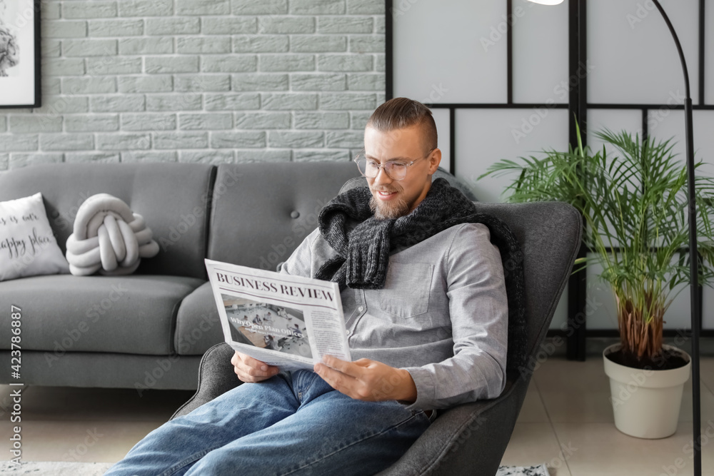 Young man reading newspaper while sitting in armchair at home Young man reading newspaper while sitting in armchair at home