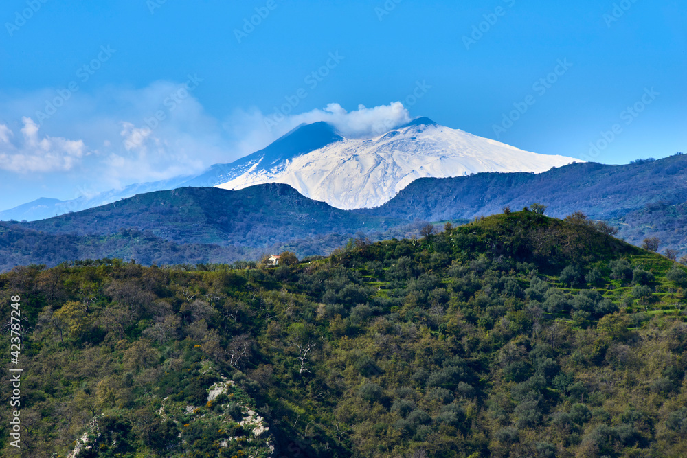 green slopes under the Etna volcano Snow-covered in a beautiful early spring sky