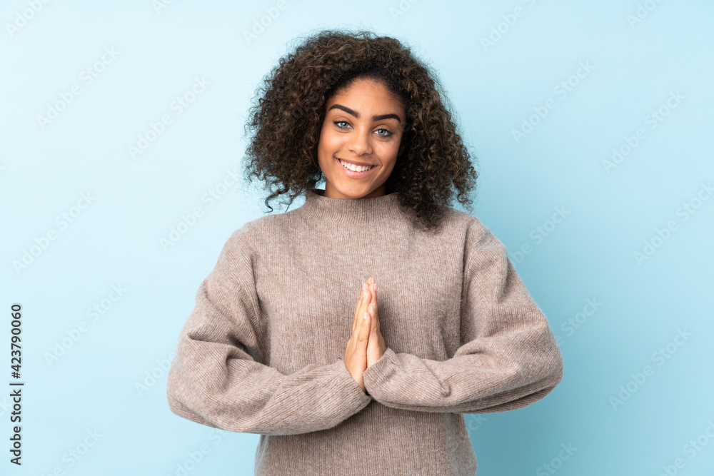 Young African American woman isolated on blue background keeps palm together. Person asks for something Young African American woman isolated on blue background keeps palm together. Person asks for something