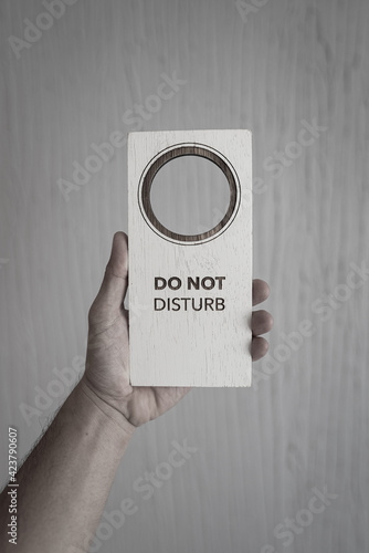 "Do not disturb" sign wooden plate is holding on people hand. Photo in gray color shade. Sign and object photo.