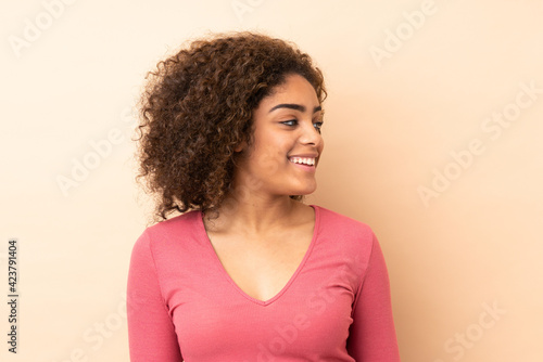 Young African American woman isolated on beige background looking side