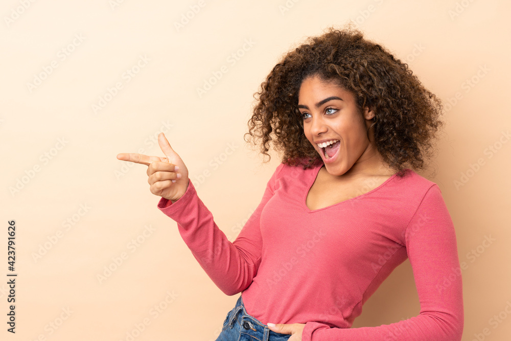 Young African American woman isolated on beige background pointing finger to the side and presenting a product Young African American woman isolated on beige background pointing finger to the side and presenting a product