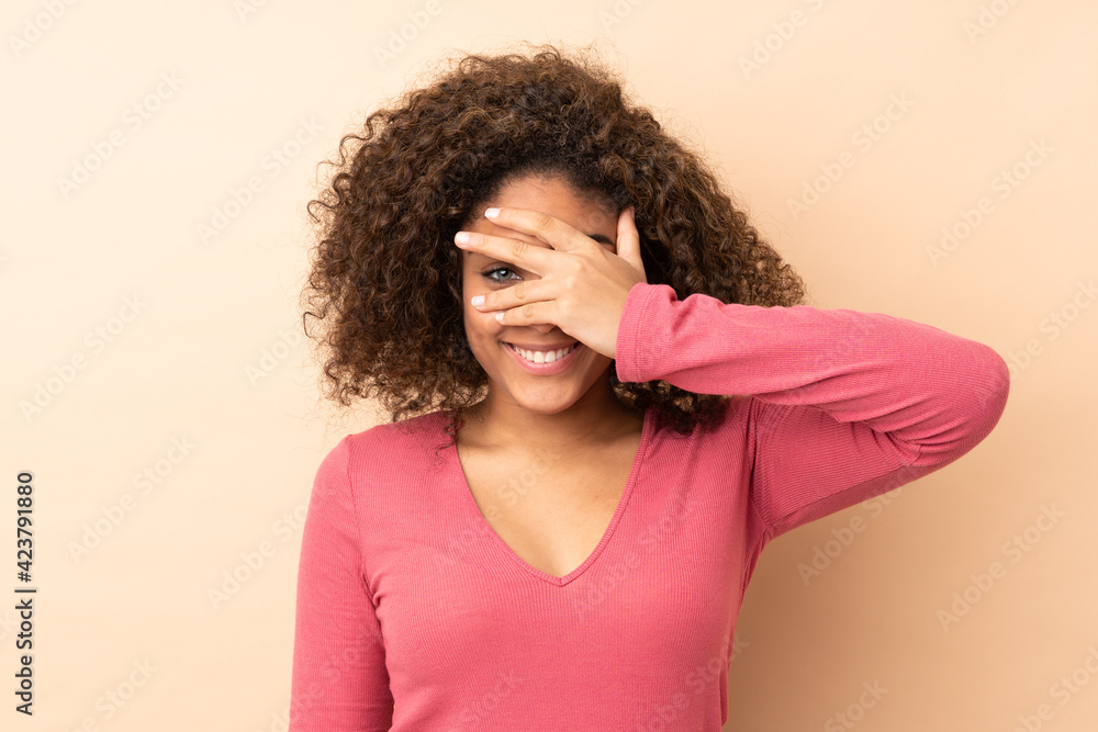 Young African American woman isolated on beige background covering eyes by hands and smiling Young African American woman isolated on beige background covering eyes by hands and smiling