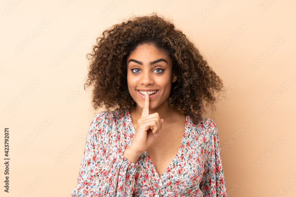 Young African American woman isolated on beige background showing a sign of silence gesture putting finger in mouth Young African American woman isolated on beige background showing a sign of silence gesture putting finger in mouth