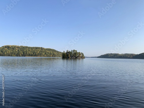 Beautiful lake scenery on a calm summer day with islands in the horizon. The sky is blue and there are no clouds. Concepts of summer holiday and peace of mind.