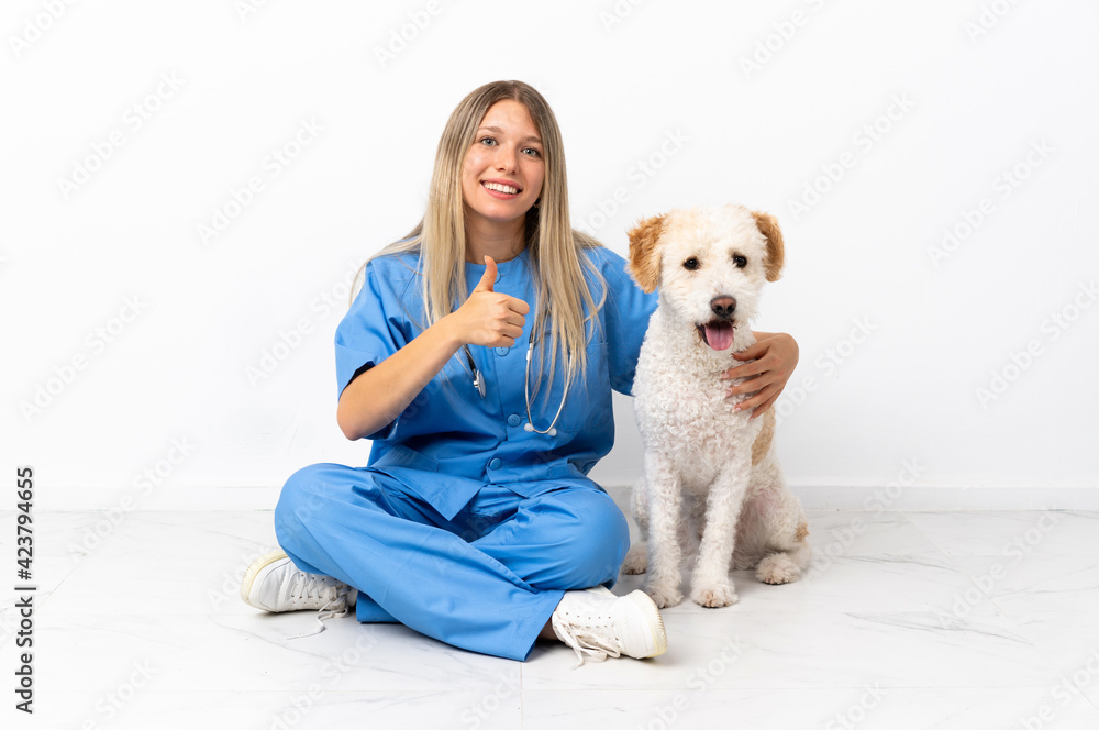 Young veterinarian woman with dog sitting on the floor giving a thumbs up gesture