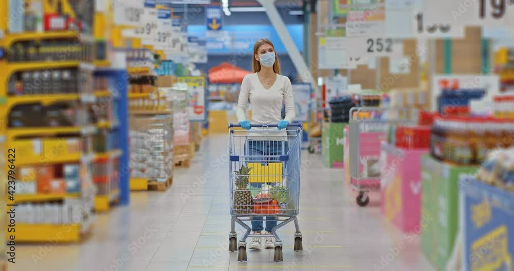 Young woman rolls a grocery cart with goods in a supermarket. Woman in ...
