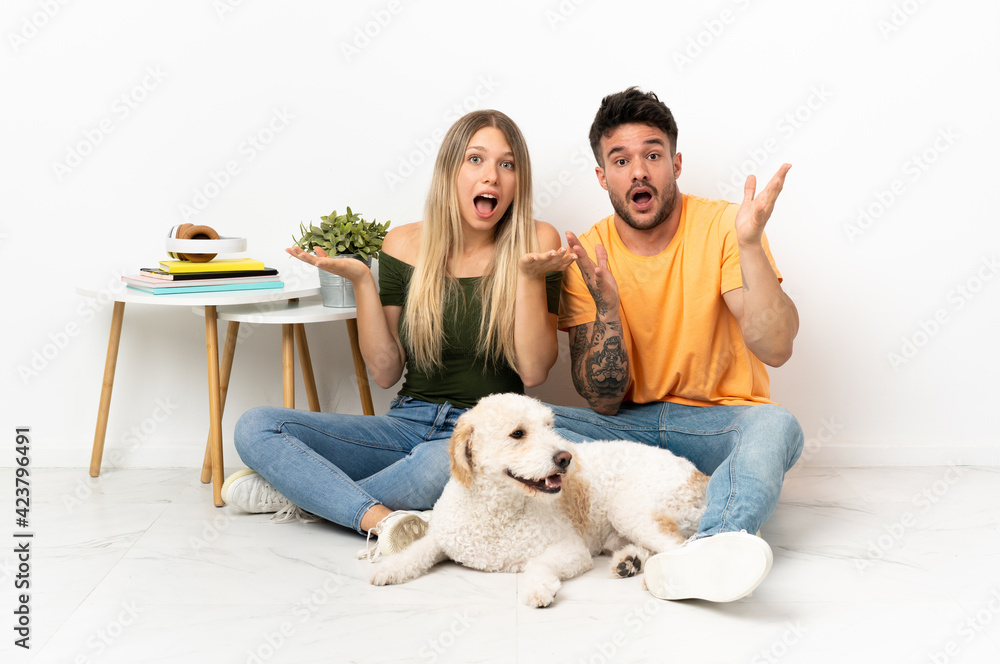 Young caucasian couple with dog staying at home with surprise and shocked facial expression Young caucasian couple with dog staying at home with surprise and shocked facial expression
