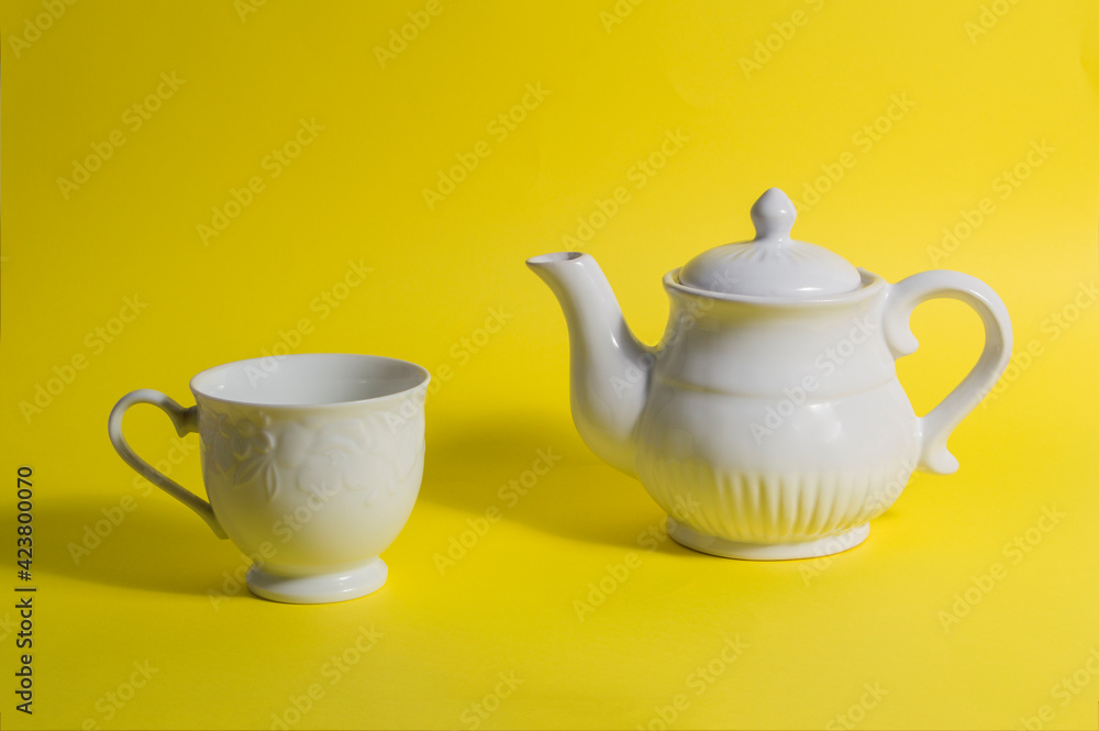 white ceramic teapot and cup, isolated on yellow background white ceramic teapot and cup, isolated on yellow background