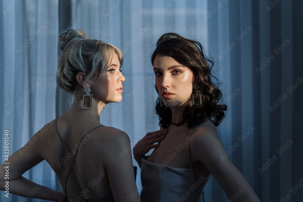 Fototapeta premium Studio portrait blondes and brunettes. Brunette watching at the camera, blonde aside. Focus on the brunette.