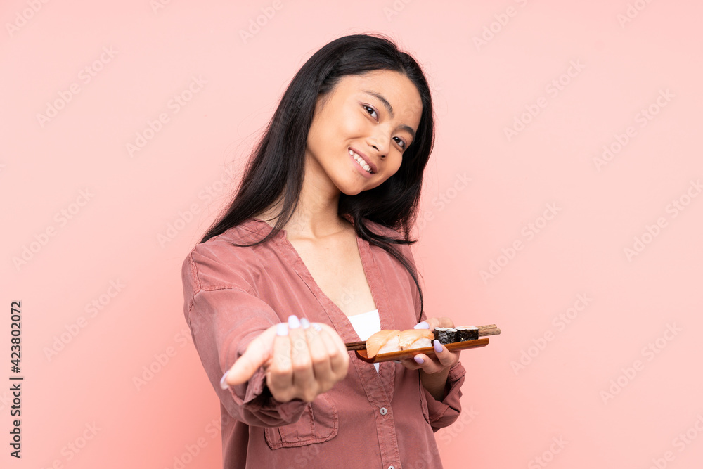 Teenager Asian girl eating sushi isolated on pink background inviting to come Teenager Asian girl eating sushi isolated on pink background inviting to come
