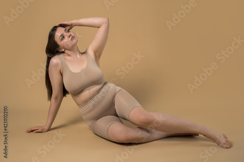 Plus size woman with folds at her body posing at the studio