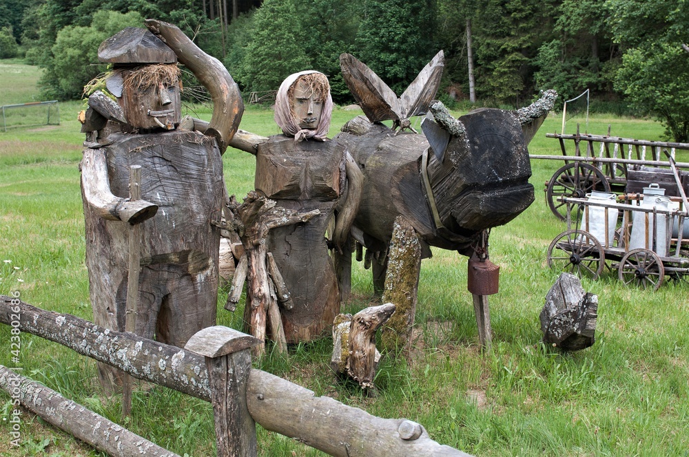 Grob , mit einer Motorsäge gefertigte Holzarbeit als Dekoration auf einer Wiese an einem Wanderweg - Bauernpaar mit einem Ochsen