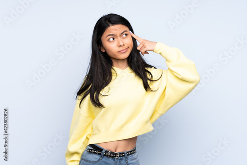 Teenager Chinese woman isolated on blue background making the gesture of madness putting finger on the head photo