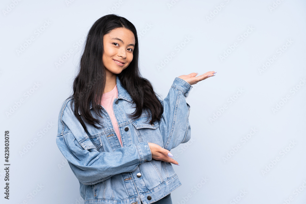 Teenager Chinese woman isolated on blue background extending hands to the side for inviting to come Teenager Chinese woman isolated on blue background extending hands to the side for inviting to come