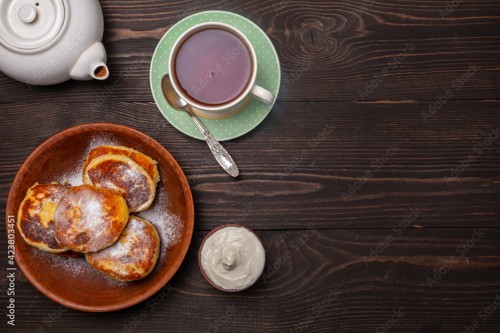 breakfast with tea and cheesecakes sprinkled with powdered sugar and sour cream top view breakfast with tea and cheesecakes sprinkled with powdered sugar and sour cream top view