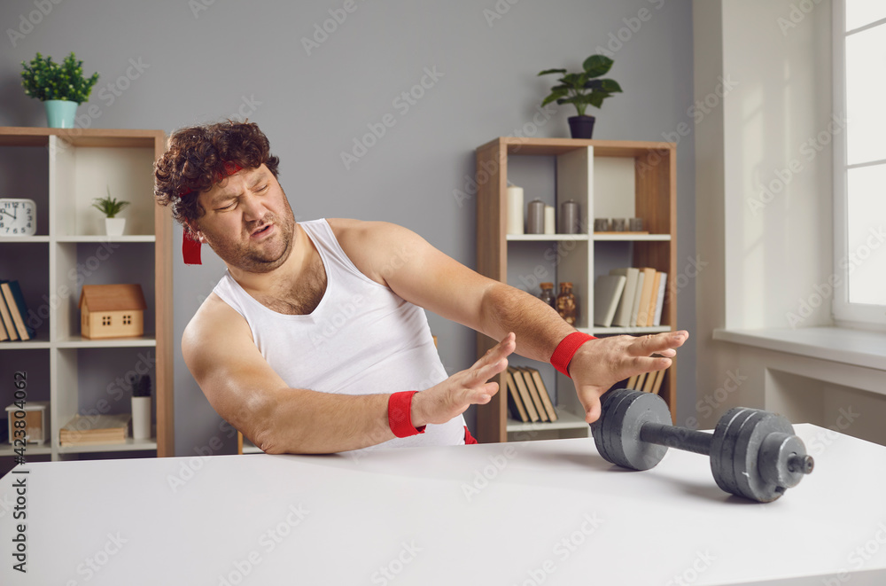 I don't want to exercise. Displeased guy pushing away fitness dumbbells.  Funny lazy chubby man feeling repulsed and disgusted at sight of sports  equipment unwilling to start gym training workouts Stock Photo