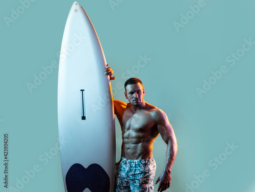 Serfer man with surfboard. Surfing hobby concept. Active lifestyle. Male beach leisure, summer vacation. Sexy muscular surfer with a surfboard. Summer boy, isolated on blue. photo