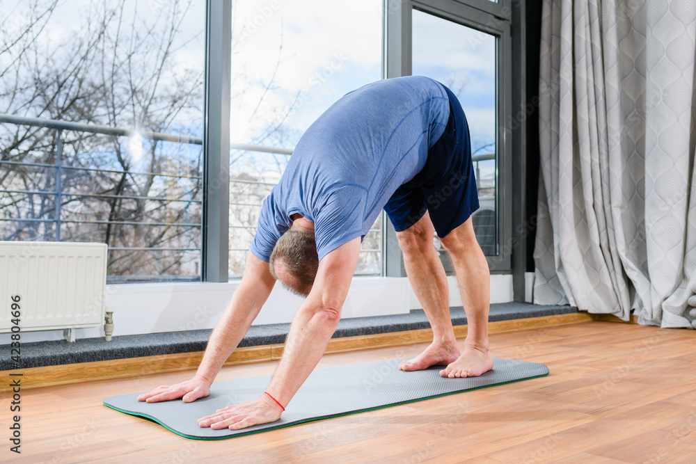 MIddle age man stay on floor mat, making workout yoga training in dog pose, tild and bend body muscles at light fitness studio. MIddle age man stay on floor mat, making workout yoga training in dog pose, tild and bend body muscles at light fitness studio.