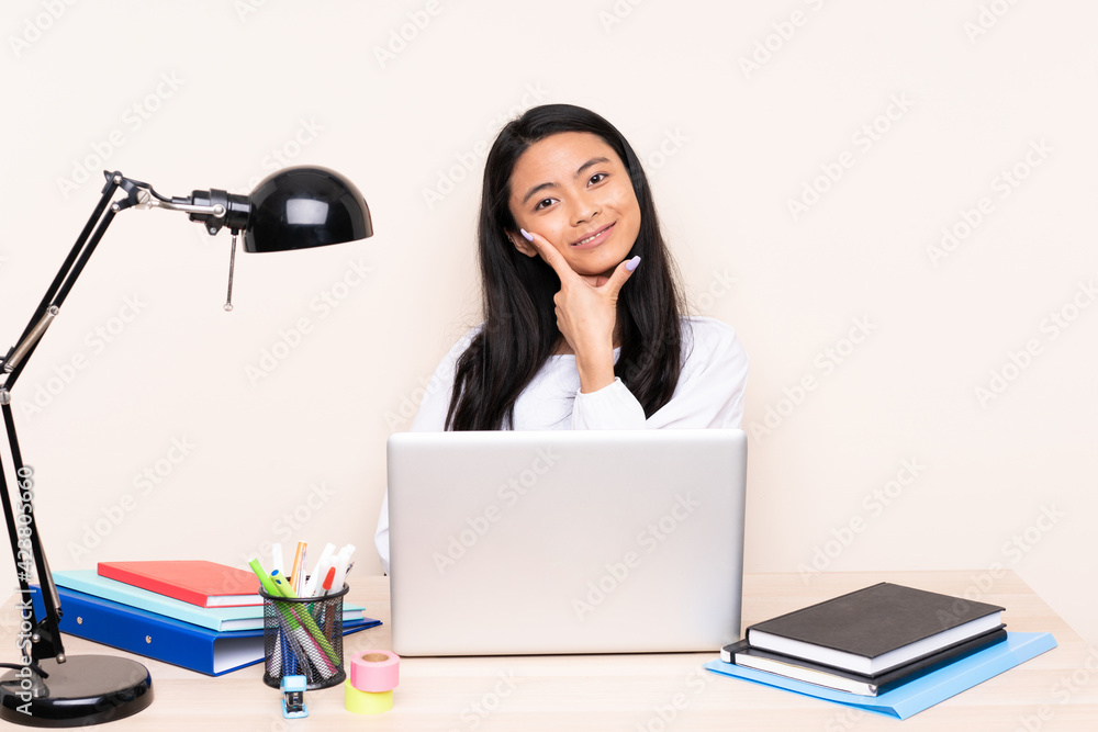 Student asian girl in a workplace with a laptop isolated on beige background smiling Student asian girl in a workplace with a laptop isolated on beige background smiling