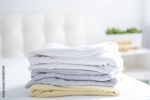 stack of women colorful sweatshirts, hoodies in pastel colors on white bed. Seasonal shopping, laundry, vacation concept