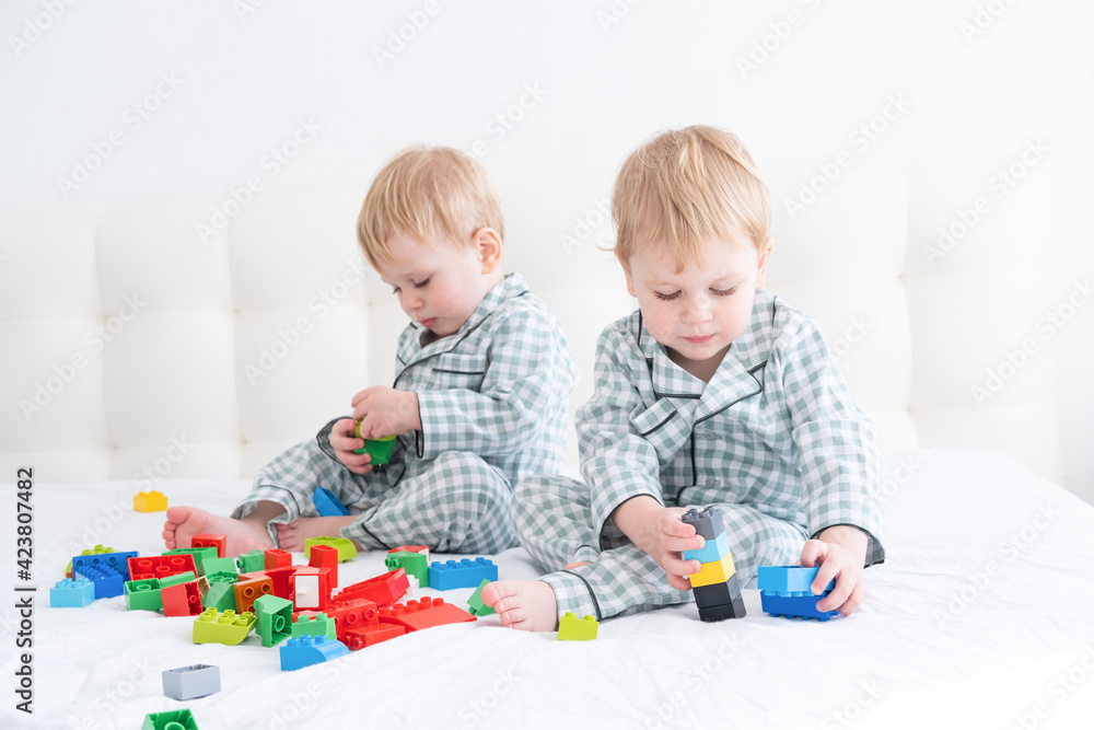 Two funny boys brothers twins on white bed in pajamas playing in constructor. Two funny boys brothers twins on white bed in pajamas playing in constructor.