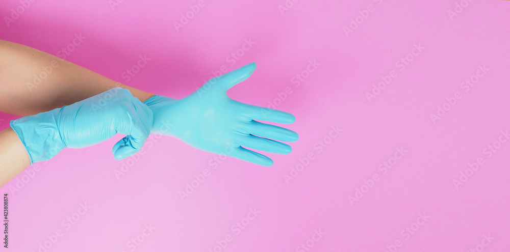 Hand is pulling blue latex gloves on pink background.
