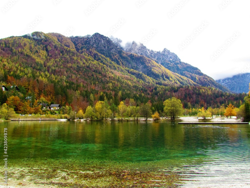 Green colored Jasna lake near Kranjksa Gora in Gorenjska, Slovenia with mountains covered in forest in beautiful autumn colors behind