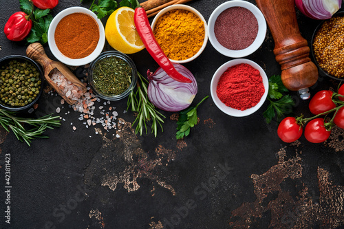 Set of Indian fragrant spices and herbs on a black stone background. Turmeric  dill  paprika  cinnamon  saffron  basil and rosemary in a spoon. Top view. Mock up.
