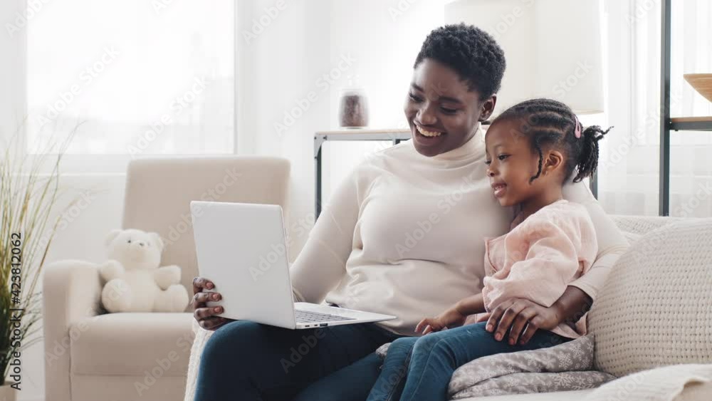 Afro american mother mom woman and little black African girl daughter child kid sitting at home using laptop computer app, talking to webcam, making online call chat conference, watching video online Afro american mother mom woman and little black African girl daughter child kid sitting at home using laptop computer app, talking to webcam, making online call chat conference, watching video online