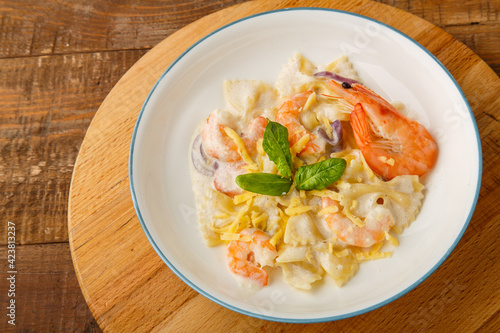 Farfalle pasta with shrimps in a creamy sauce on a gray plate on a wooden table on a round wooden stand.
