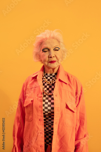 Woman dressed in stylish coat posing at the studio with eyes closed