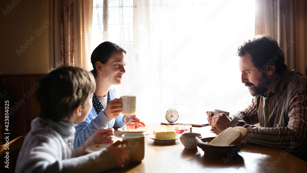 Portrait of poor sad small girl with parents eating indoors at home, poverty concept. - obrazy, fototapety, plakaty 