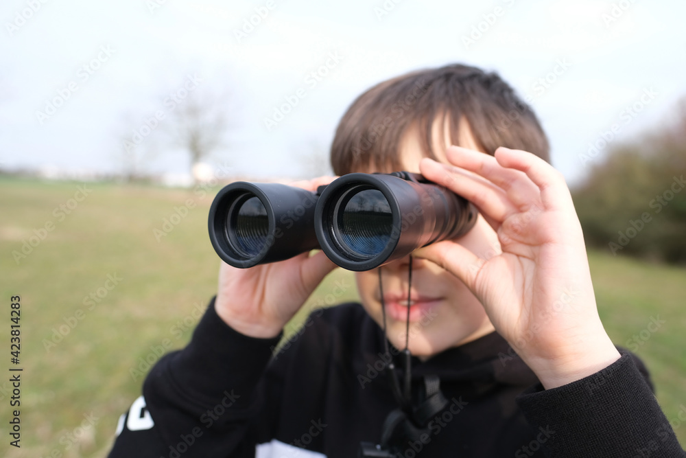boy, guy 8-10 years old stalker looks through black binoculars in the park, spies, hunts down secrets, the concept of surveillance, observation of people and animals