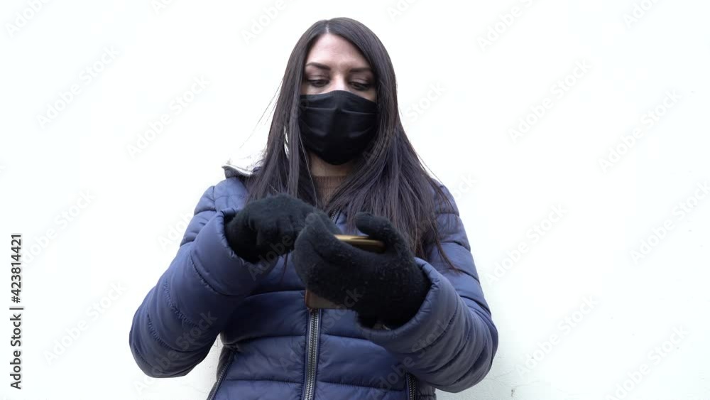 young woman outdoors with winter clothes and health mask while using her smartphone young woman outdoors with winter clothes and health mask while using her smartphone