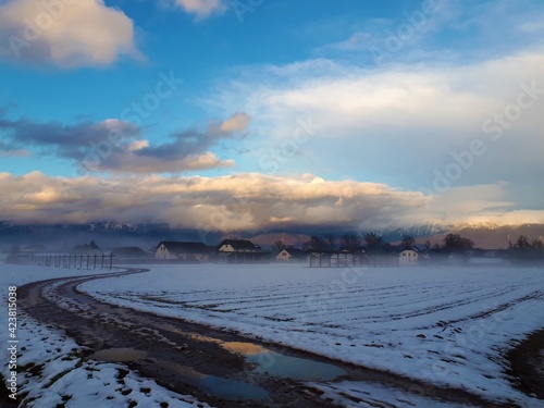 Scenic view of mountains covered in clouds lit by sunlight at sunset and snow covered field and a village at Sorsko polje, Gorenjska, Slovenia photo