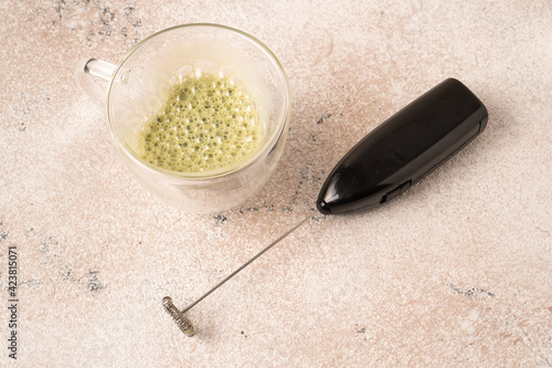 Green matcha latte with bubbles and small handheld drink mixer. Homemade green matcha tea and electric frother